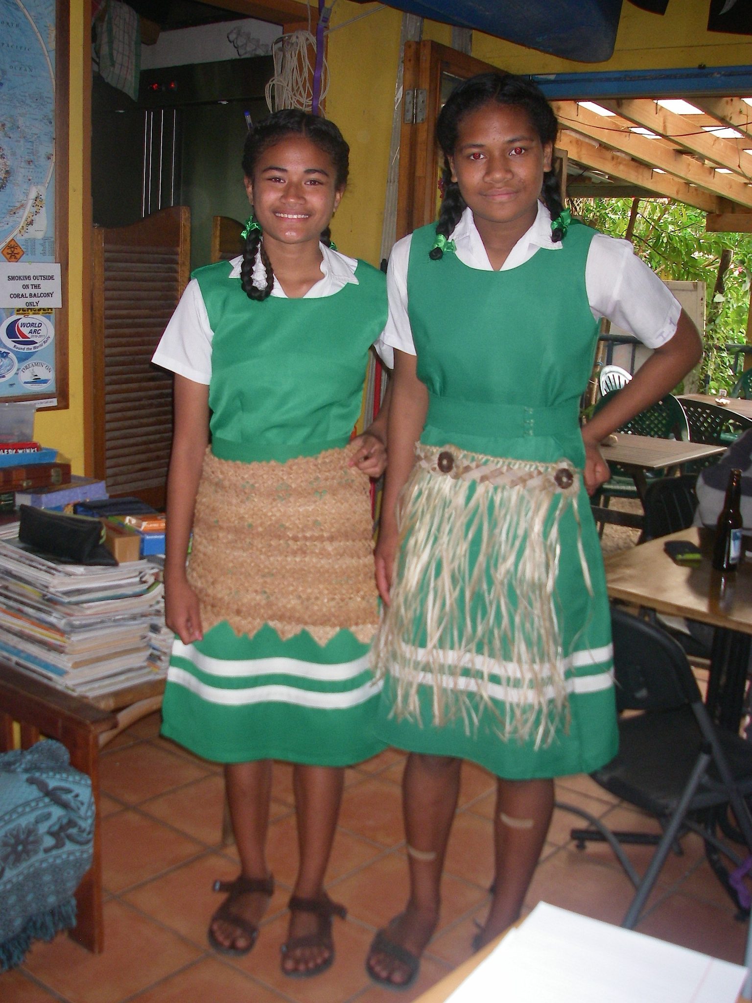 32. Two beautiful Tongan school girls wear over their school uniforms two styles of traditional garments to show homage to the monarchy of Tonga