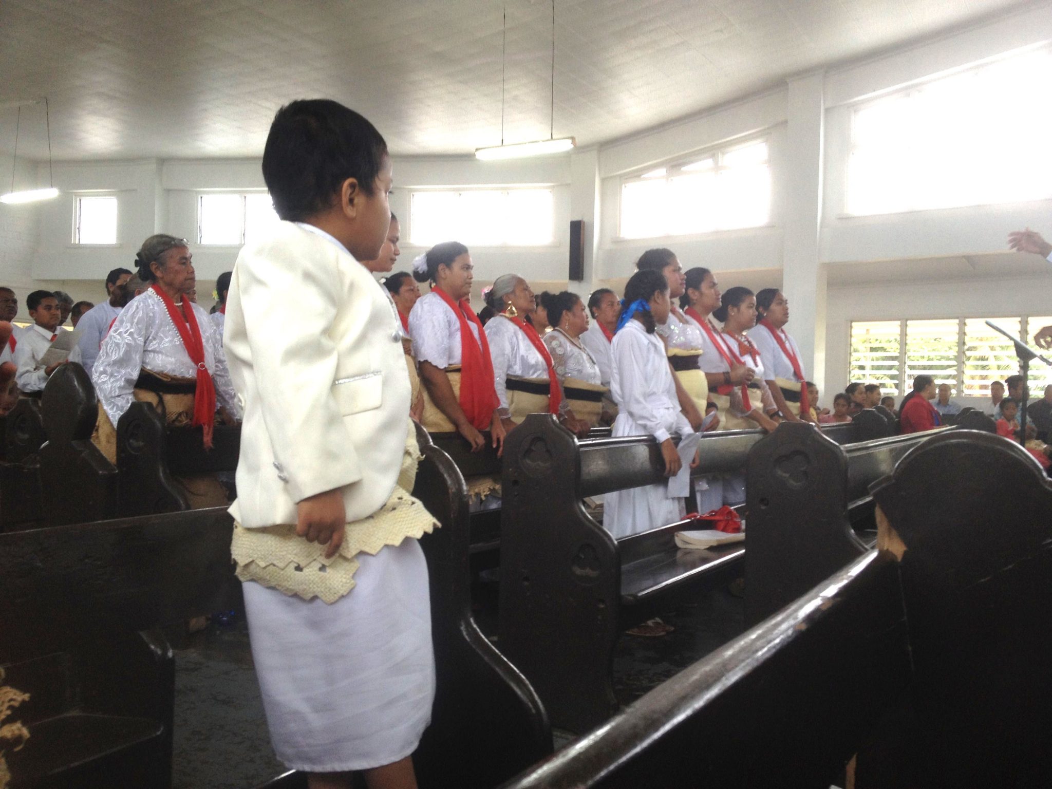 8. In the Free Wesleyan Church of Tonga, a young lad wears a Tongan sarong covered with the woven wrap signifying allegiance to the crown of Tonga. The choir in the background and most of the congregation also wore these traditional garments